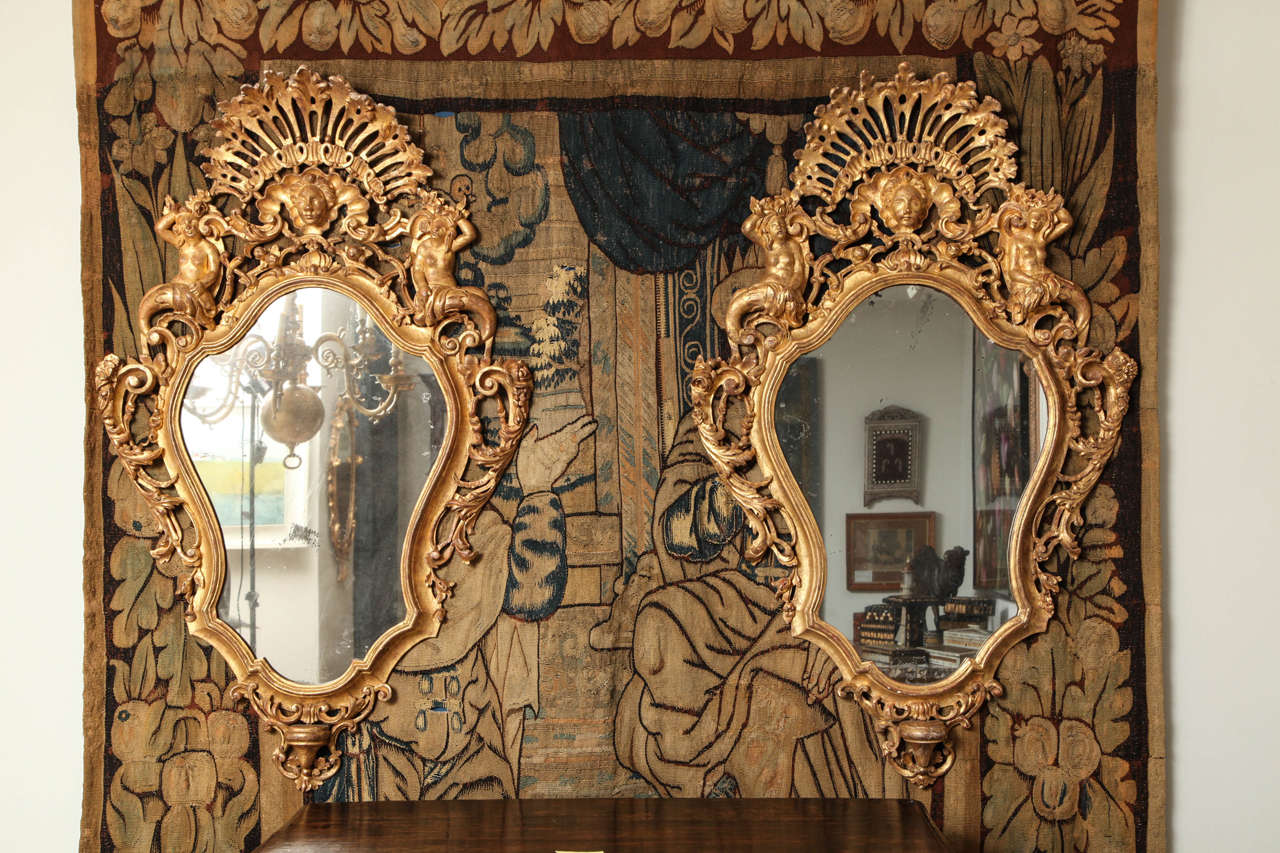 Fine pair of Continental giltwood mirrors with elaborate pierce carved fan crestings over central masks, each supported by a pair of mermaids, the cartouche shaped mercury glass plates with molded borders surmounted with foliate and scroll carving,