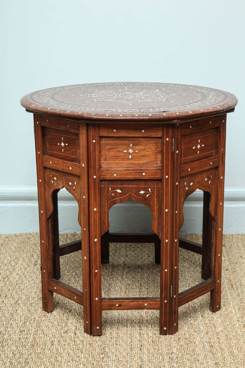 Fine Indian bone inlaid sandalwood table, the circular top with ebony ringed stringing and inlaid bone floral and sunburst decoration, the base with inlaid decoration and arched brackets and having accordion action folding ability. Almost always