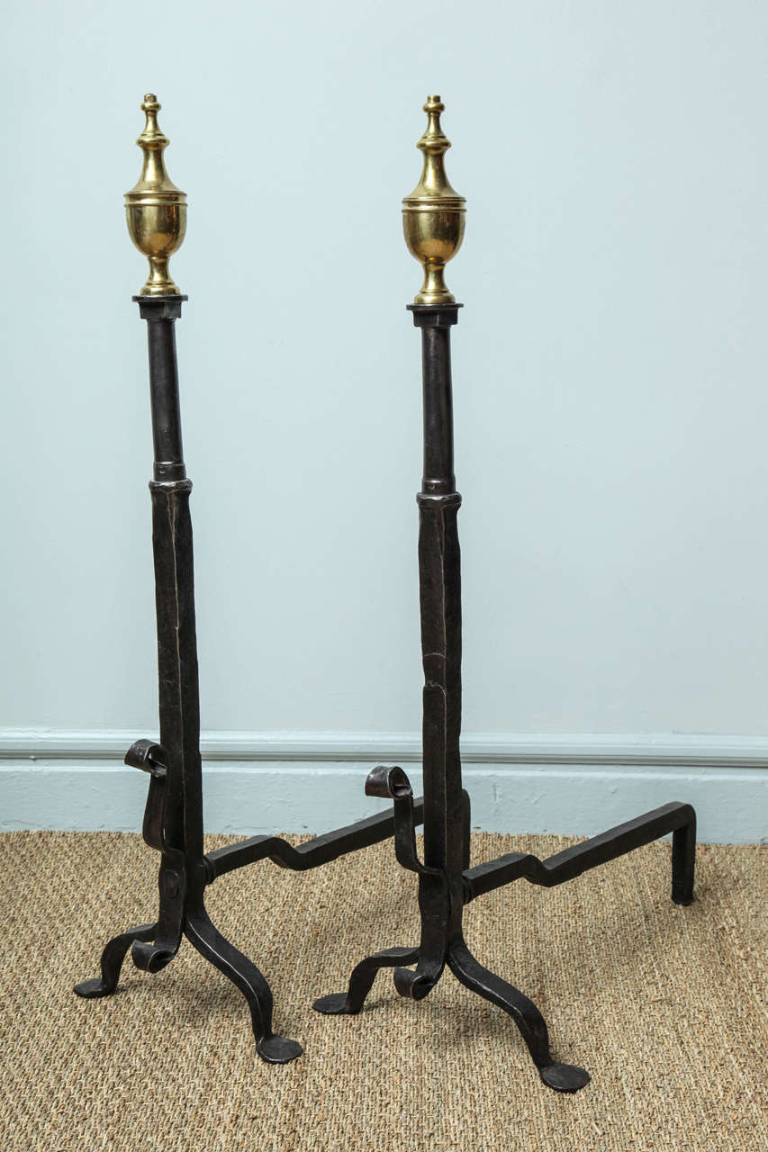 Good pair of brass and wrought iron andirons, the urn finials over hand hammered shafts, the upper section cylindrical, the lower section square divided by ringed collar,  standing on low arched legs ending in penny feet and having decorative