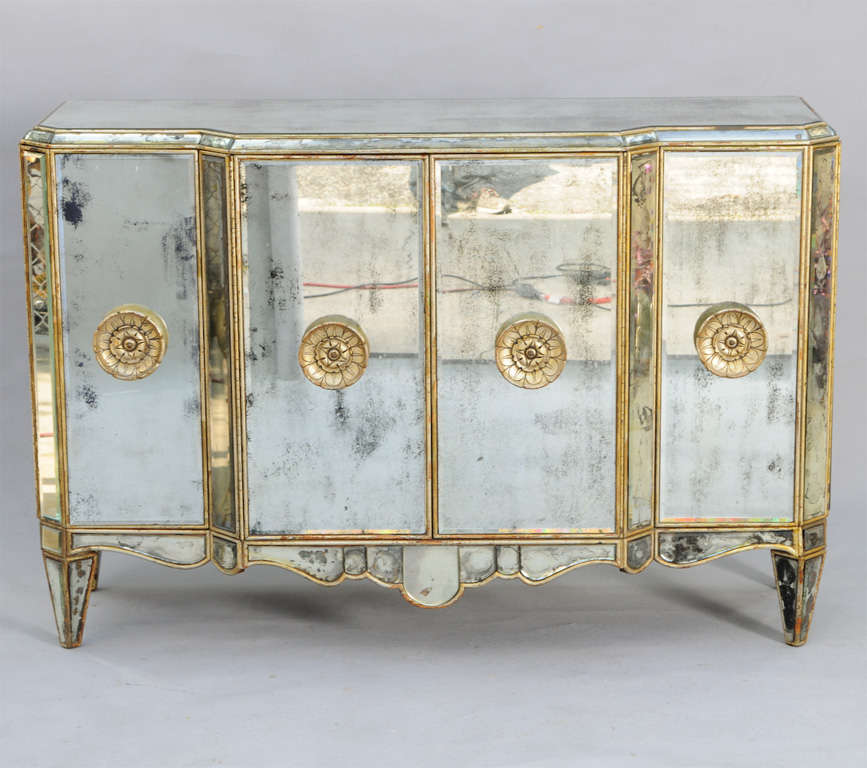 Spectacular credenza, having a breakfront shape, all surfaces covered in bevelled distressed mirrored panels inset into silvergilt frames; four cupboard doors centered by wooden rosette handles, over shaped apron, raised on square tapering pegs