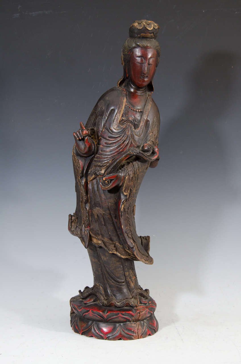 A beautiful and serene Chinese hand-carved, hardwood Guanyin statue or sculpture holding a ruyi scepter and standing full length on a double lotus. Painted with black, gold and red raised lacquer, this piece is from the late Qing Dynasty.<br />
<br