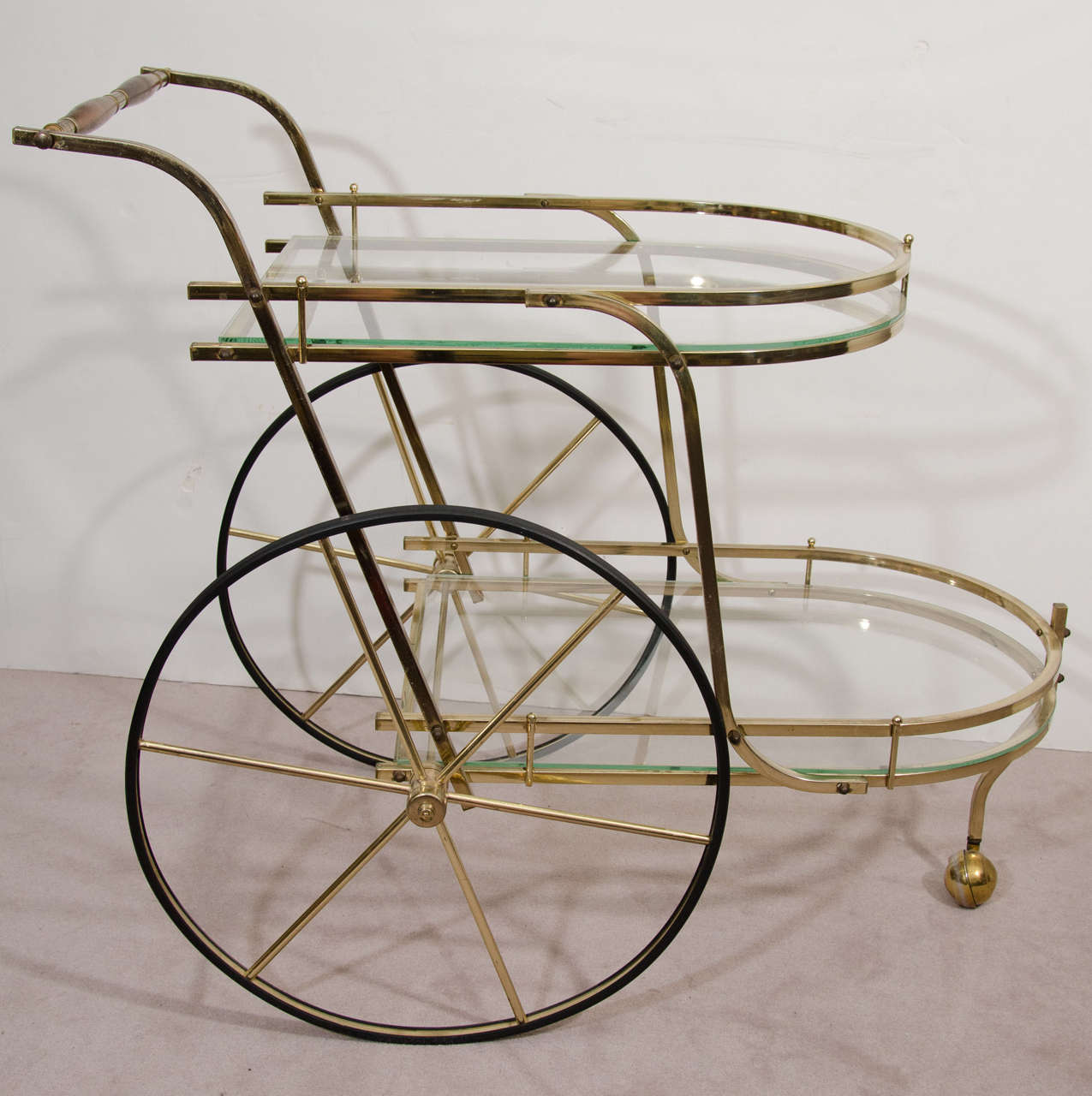 A vintage three-wheeled brass bar cart with two glass tiers, and a push cart style handle bar with wooden accents.

Good vintage condition with age appropriate wear. A few minor scratches to the glass.

Reduced from: $1,850