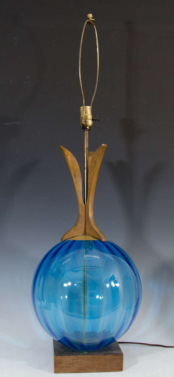 A Danish Modern table lamp with a blue undulated glass globe base, and an architectural wood and brass stem. 

The piece has its original 16" shade, and sits on a metal platform base.  Some water damage to shade.

Reduced from: $650