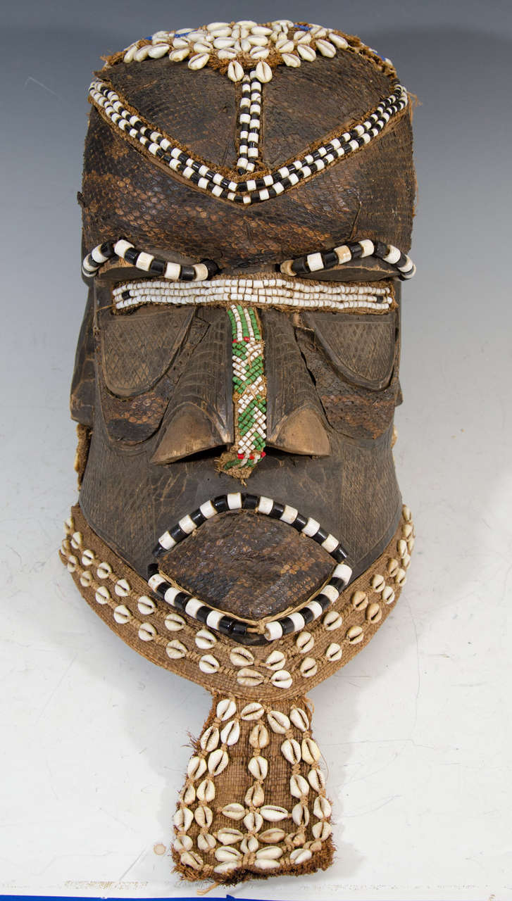 A 20th century or earlier Congo decorative tribal helmet mask adorned with shells, snakeskin, beading, and burlap. Possibly made by the Kuba people. The Kuba have used more than 20 different types of masks for various functions such as; initiation