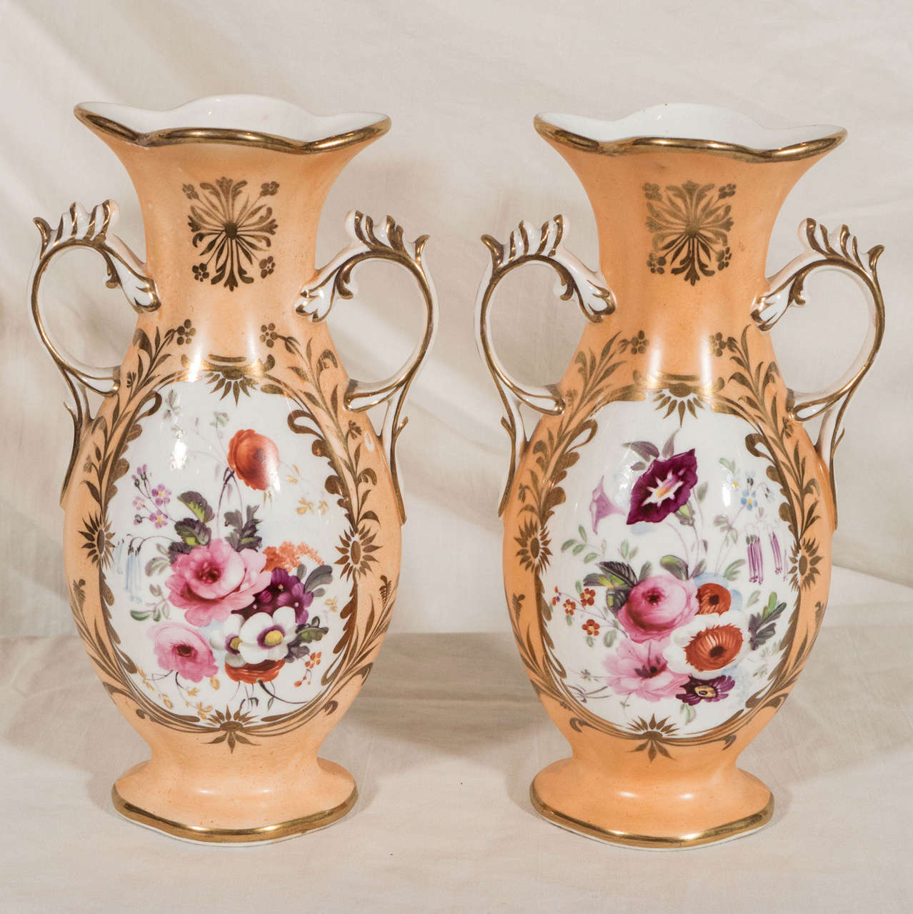 A lovely pair of Victorian bud vases delicately sculpted in an appealing shape. Painted in a soft peach tone, the centers decorated with colorful bouquets of flowers.