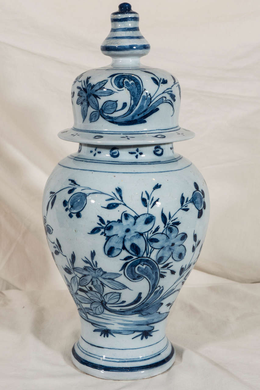 A pair of blue and white Dutch delft covered vases painted with a simple design of large flowers on the vine. The cover knop and the base are painted with traditional horizontal lines.