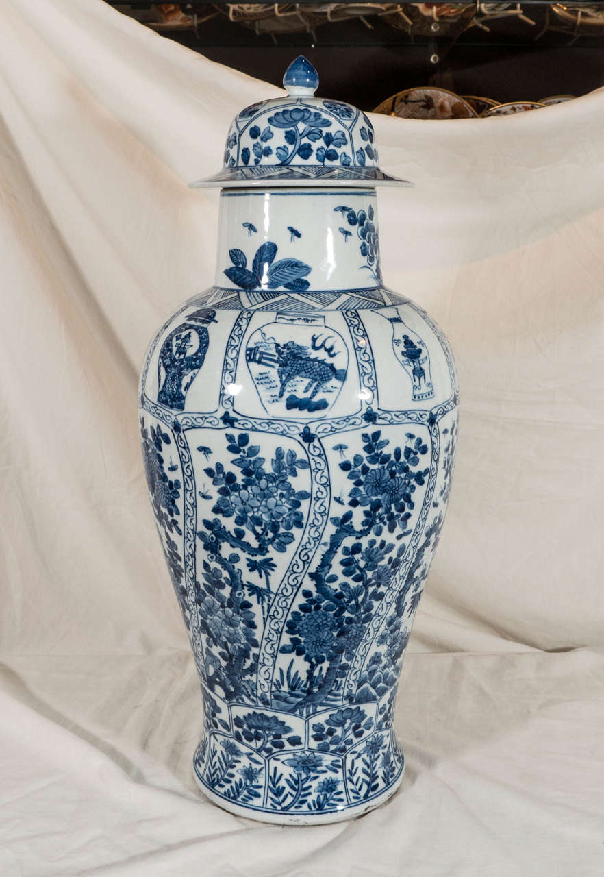 A pair of Qing Dynasty blue and white covered vases of slender shape painted in underglaze cobalt. Each decorated with rows of petal-shaped panels filled with prunus and peonies. The shoulders are decorated with images of vases, which are decorated