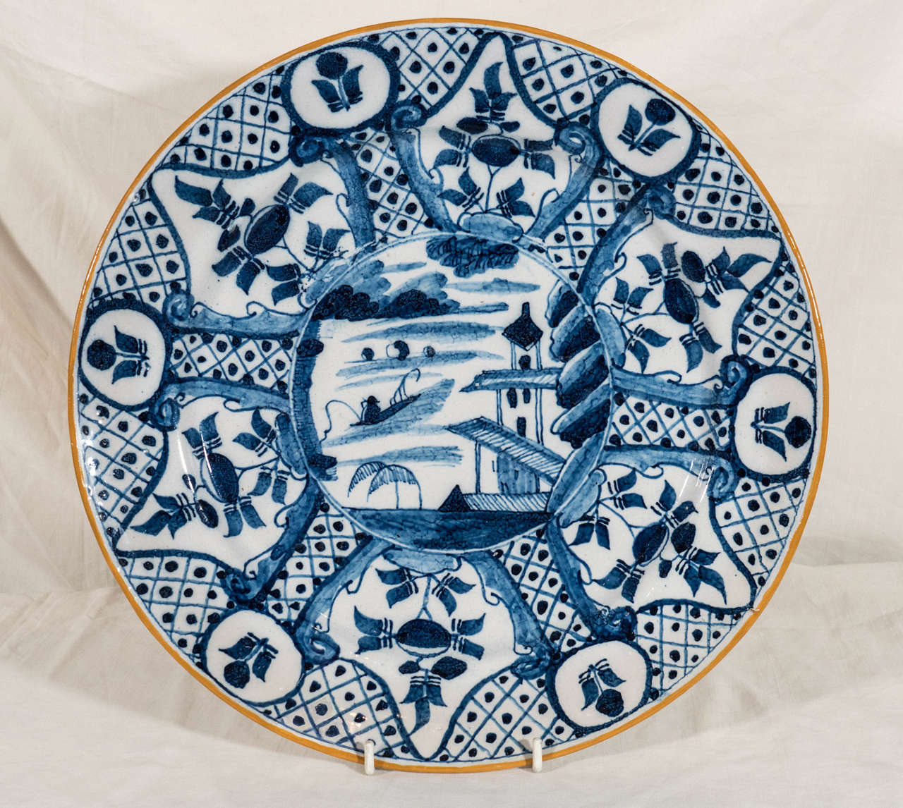 The design combines the bold brush strokes typical of Delft with the sophistication of Chinese inspired design. The central roundel shows a naive version of a chinoiserie scene with a pagoda, and small boats on the water. The dominant geometric