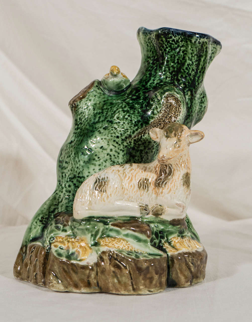 The charm of this Staffordshire spill vase is it's Folk Art style using simple forms depicting a scene from everyday country life: A lamb resting at the base of a tree. Despite the simple style of the figure the lambswool and the trunk of the tree