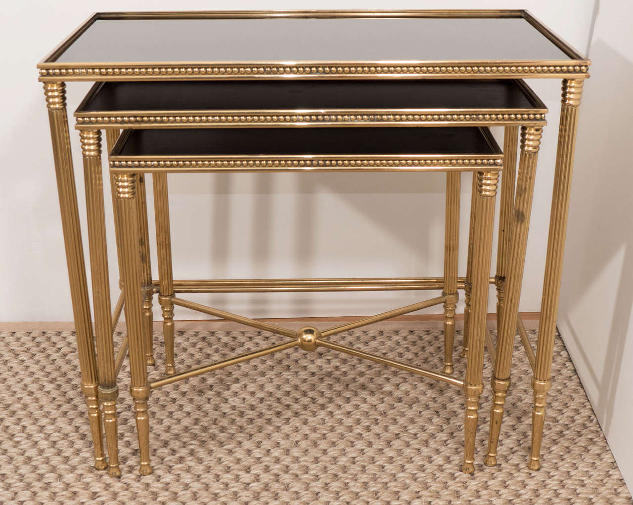 A chic set of three nesting tables, with reeded and beaded brass frames and black mirrored tops.
