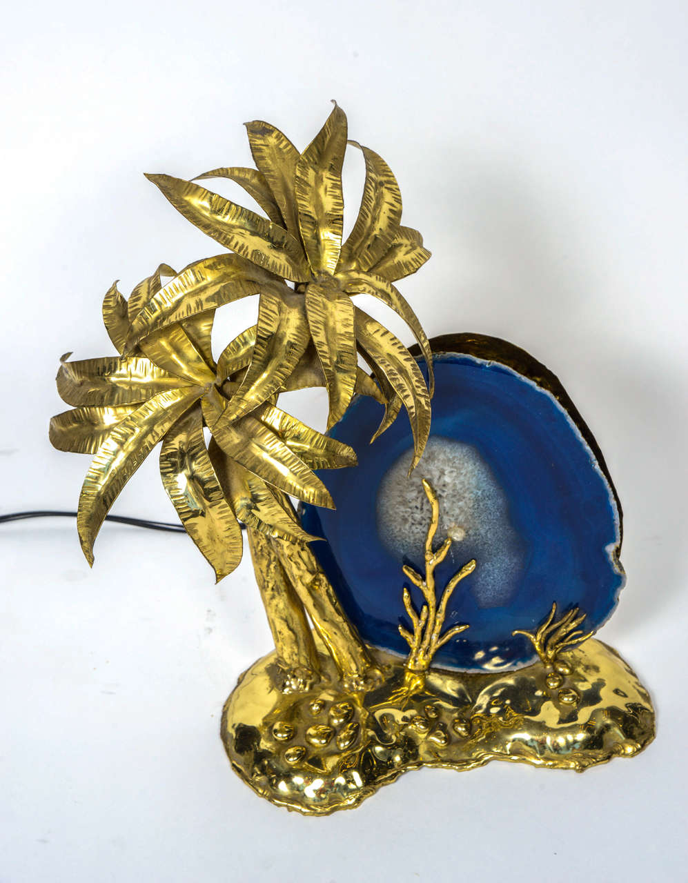 Unique lamp created by Isabelle Masson-Faure in the 1980s.

It is made of a big brass setting representing a beach with two tall palm trees and a couple of seaweeds climbing on a slice of blue agate representing the sky.