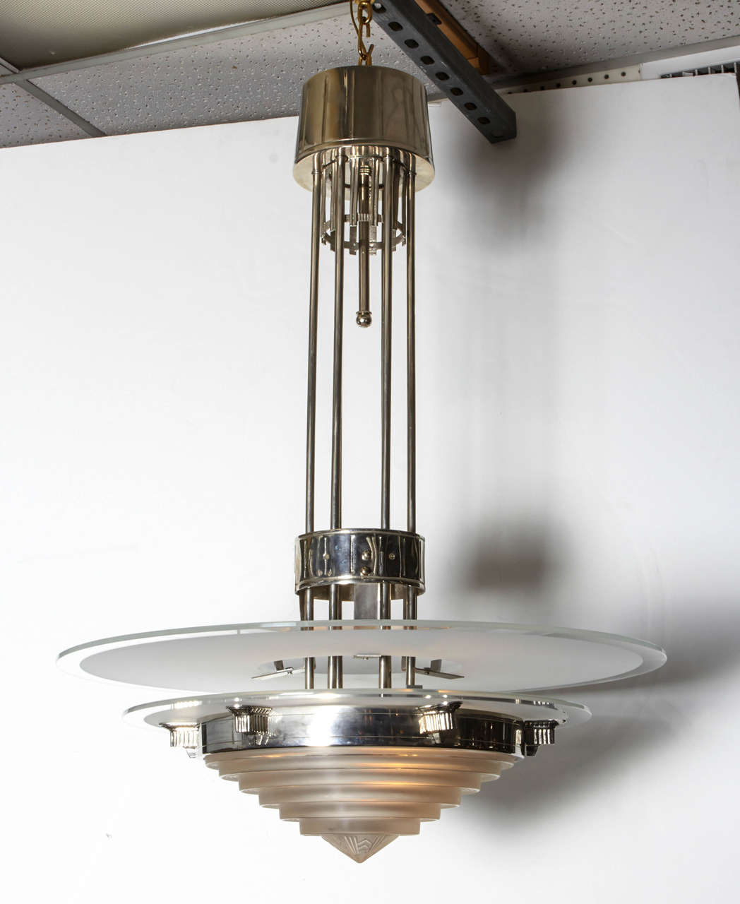 A Modernist, machine age chandelier in glass and polished nickeled bronze. Central concentric coupe and double disc top with wide supportive surround ending in a highly decorative stem and canopy.
The Industrial Design captures a Minimalist and