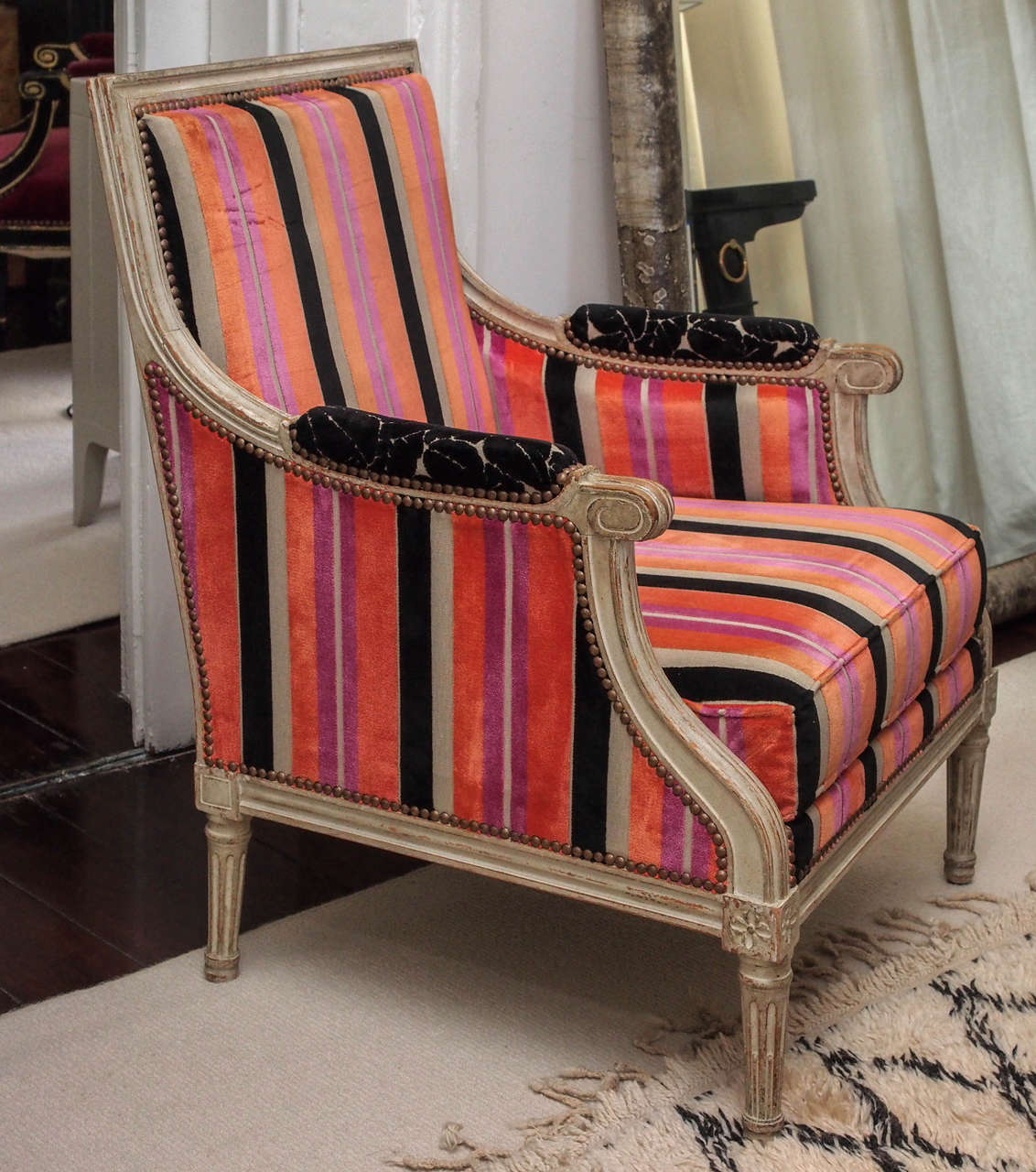 Two Louis XVI-style bergeres; the striped velvet upholstery with contrasting arm pads; tight back and loose seat cushion; the beech frame in attractively distressed 