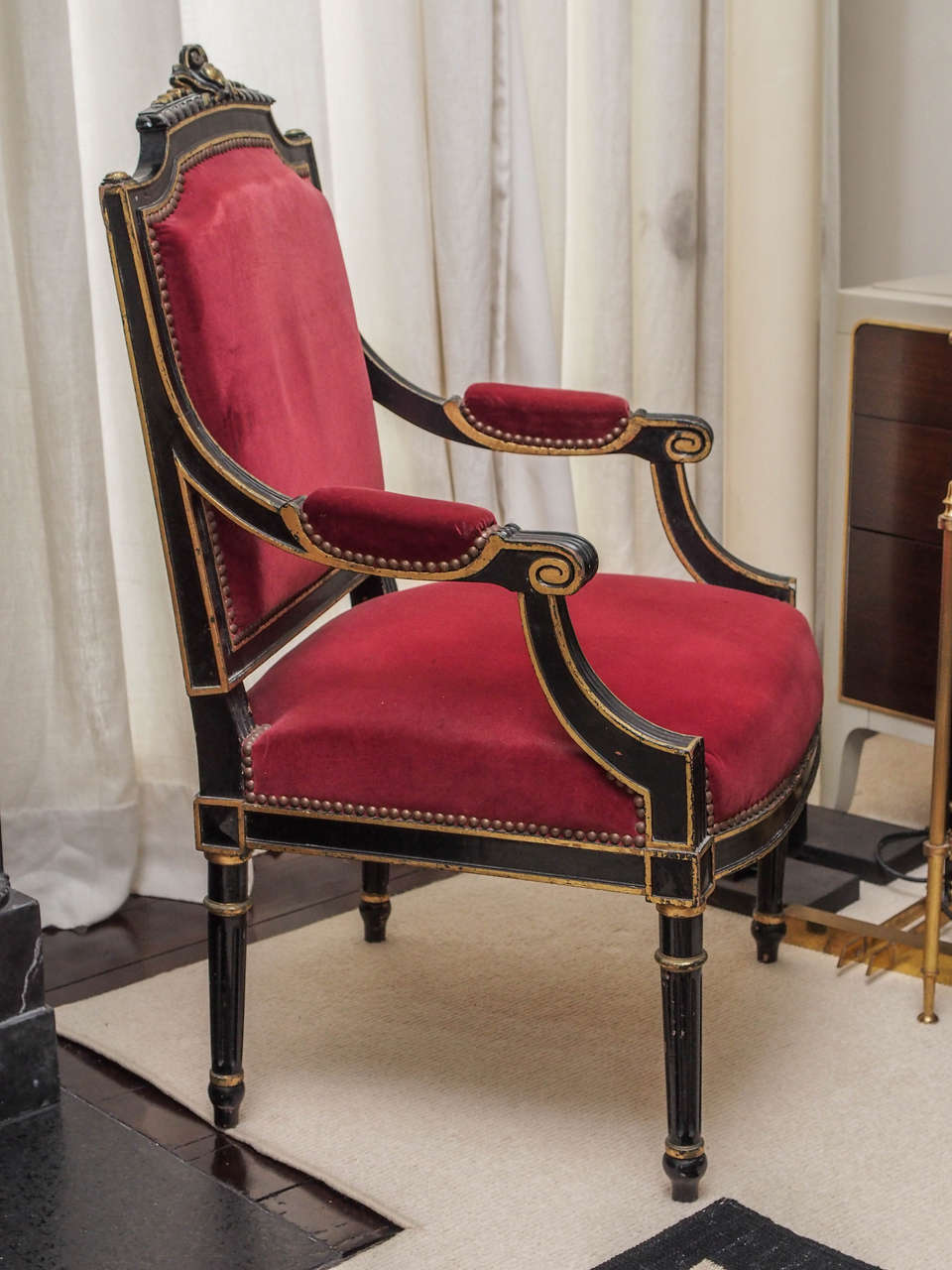 Two ebonized armchairs with gilt details throughout; red velvet upholstery with brass nailheads.