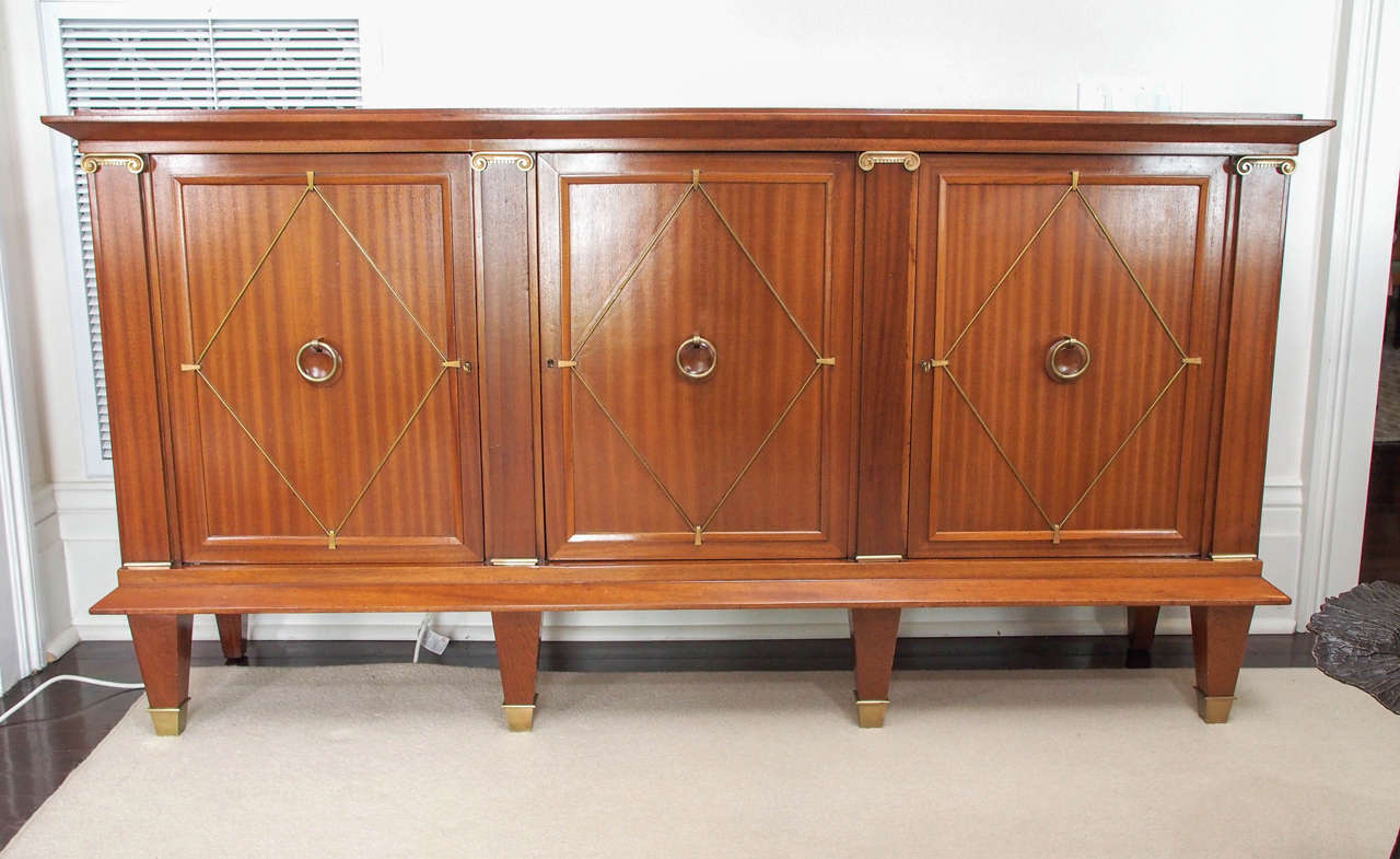 Handsome three-door sideboard in mahogany with bronze fittings, the open cabinets separated by engaged ionic pilasters, each with one adjustable shelf,
square tapered feet with bronze sabots, attractive ring pulls, working key.