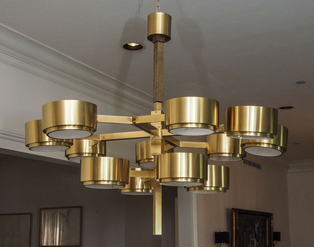 Two impressive twelve-light chandeliers in brass; opaque white glass shields the lamps.