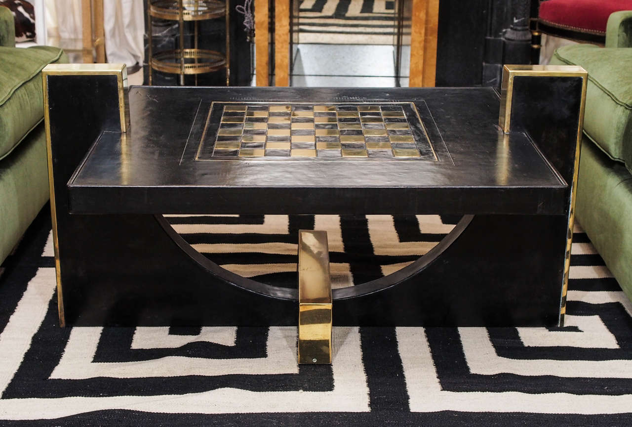 Handsome low table in black leather with inset brass chess board; interesting curved base with brass details; plateau with chess board is 17