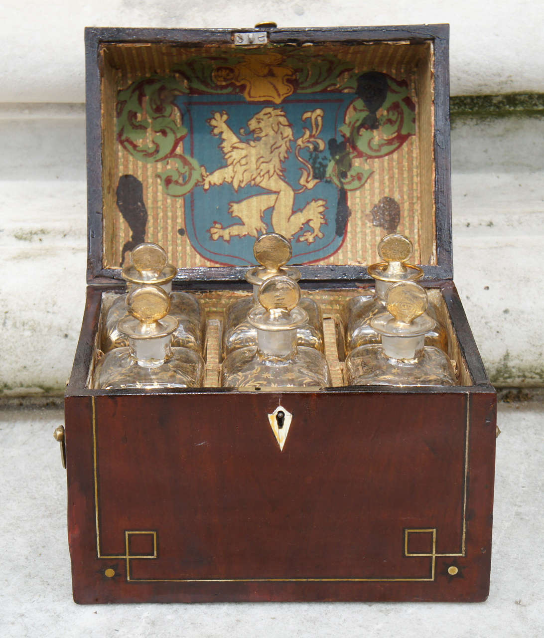 A exquisit Mohognay Box with brass inlay. It supports 6 hand blown decanters, with gold filigree design on each. Lined with original paper.