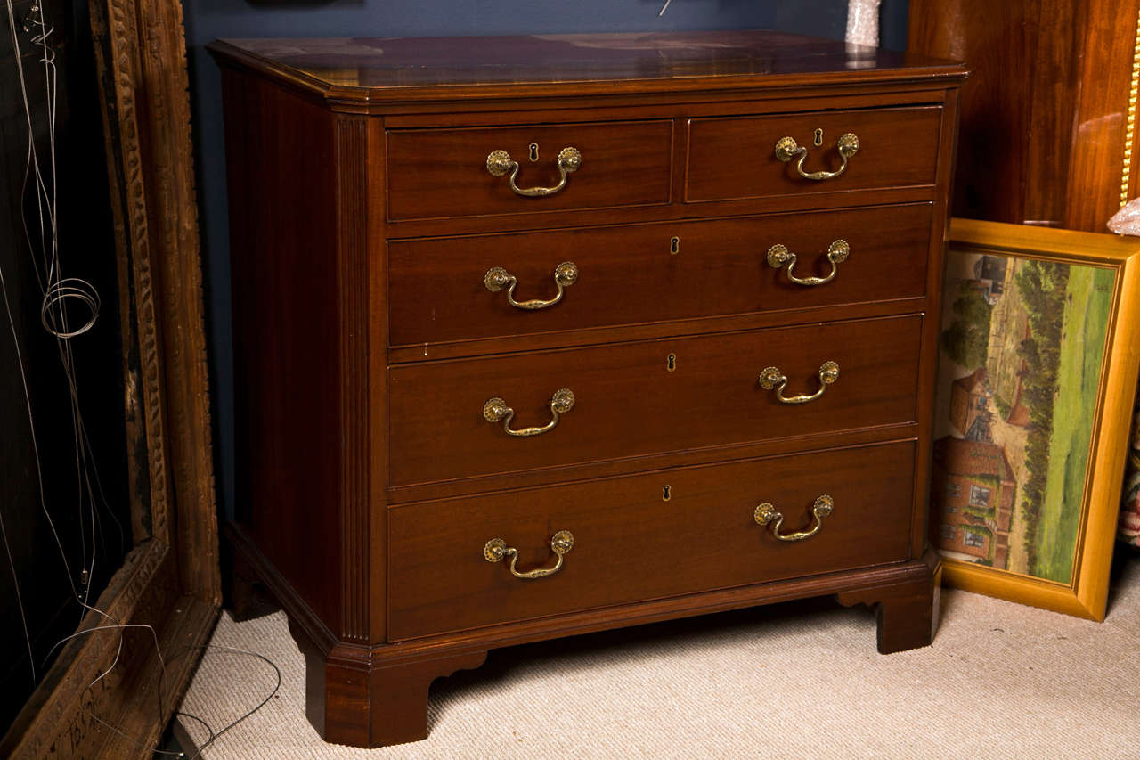 An English George III period mahogany Chippendale style chest of drawers having two short over three long cockbeaded drawer fronts, canted & reeded styles and original brasses, all resting on ogee bracket feet.