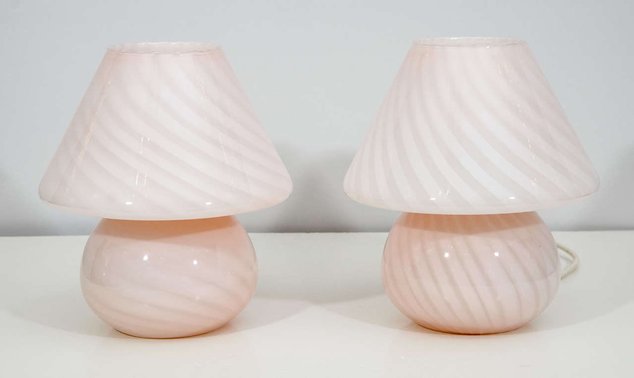 Charming pair of petite Murano lamps. The lamps are designed in the classic profile of a lamp with shade, but are in fact one handblown and formed piece of art glass. They have a very light pink color and emit a lovely glow.