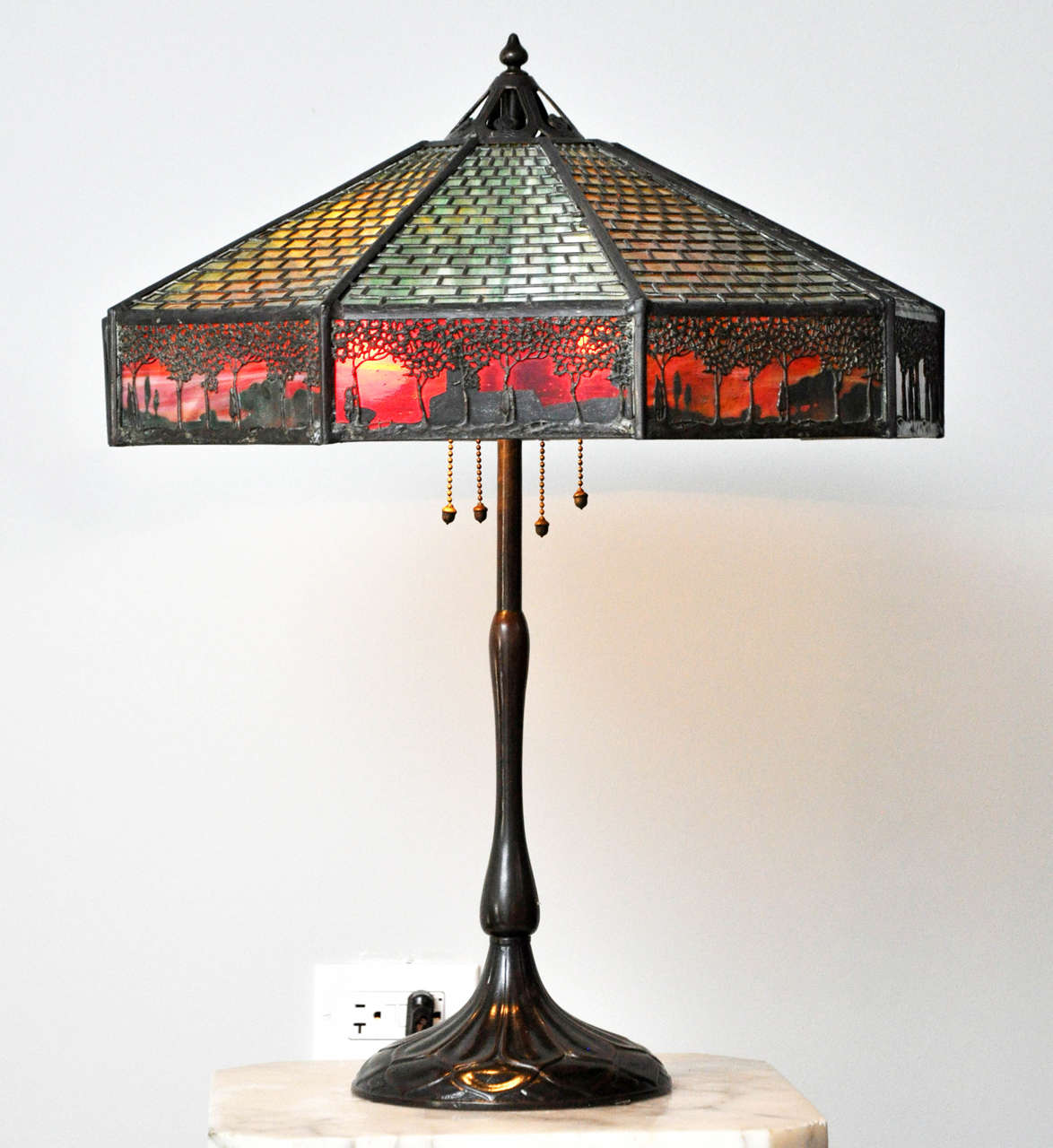 Arts and Crafts Handel "Teroca" tropical sunset table lamp. Period green slag glass with olive colored patinated metal brick overlay, nine section border of a reddish brown color slag glass representing the sunset with tropical tree scene