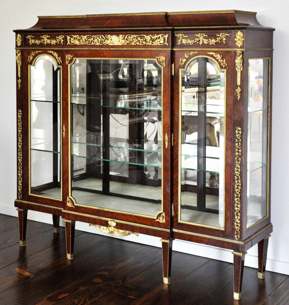 Rare Neoclassical Louis XVI Style Mahogany and Gilt Bronze-Mounted Vitrine with glass shelves and mirrored back panel. Three-part rectangular flamed mahogany Neoclassical shaped body, hand beveled square door flanked by two arched hand rectangular