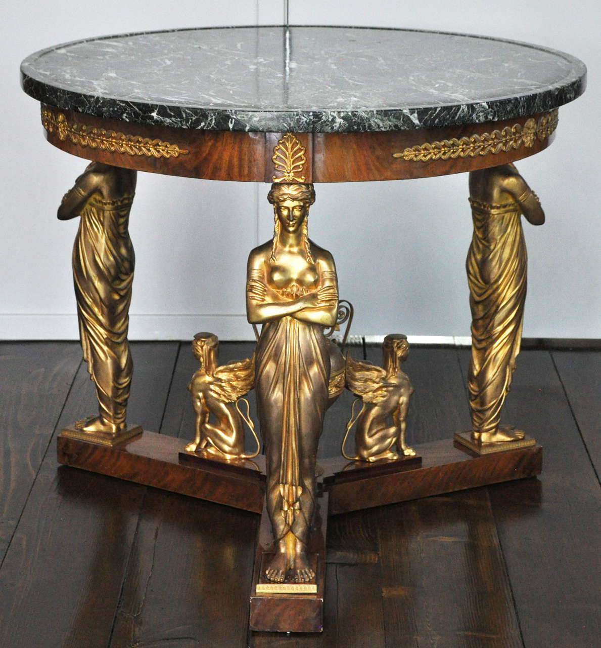 An important Empire style gilt bronze mounted mahogany salon table after a model from 1808 by Jacob-Desmalter. Circular verde antico marble top surface above a mahogany frame, the frieze mounted with laurel leaf banding alternating rosettes and