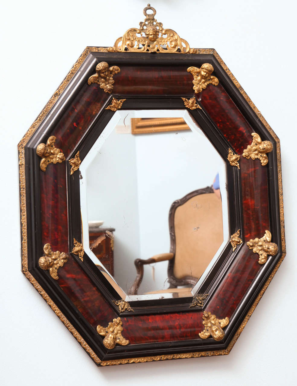 A tortoiseshell octagonal mirror with applied gilded bronze putti with foliate motif on the crown (cimasa) and eight larger gilded bronze putti in the corners, eight small winged motif on the interior corners; with ebonized molding and gilded bronze
