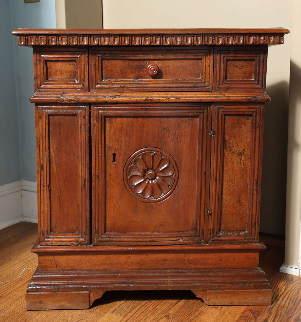 A walnut credenzina with a rectangular top above dentil carved molding above one drawer in the center; with a long door on the front, the door with carved rosette; resting atop a plinth base.
Tuscany, Italy, early 17th century