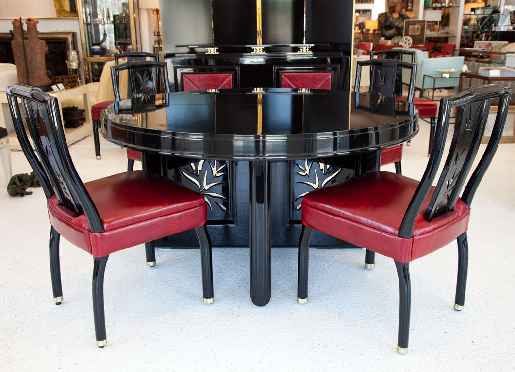An incredible round black lacquered Asian inspired dining table and six upholstered red leather chairs with brass sabots designed by James Mont.  Stylized bamboo cut outs complete the look. Table has 2 12