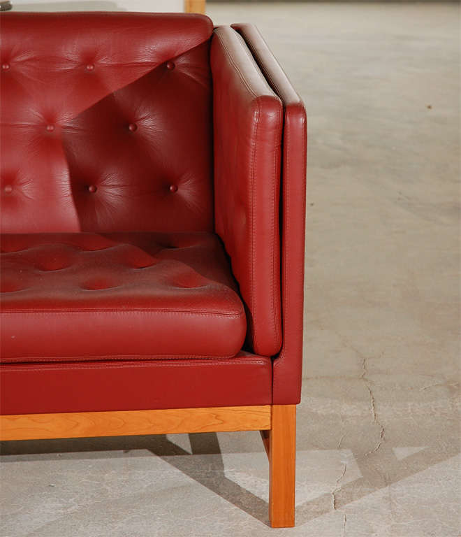 Red leather sofa with tufted seat and back, and a wood base.