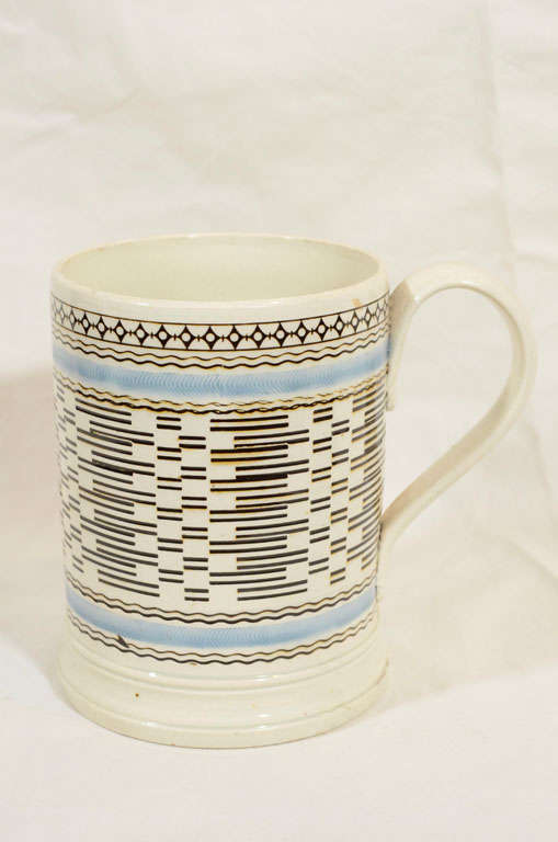An English Mochaware mug, machine turned, with herringbone bands of light blue above and below an overall design of dashes, diamond shapes, straight and wavy lines painted in black