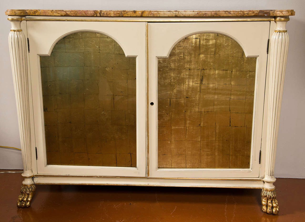 Pair of Regency style cabinets, each has a shaped marble over a white painted and parcel-gilt conforming cabinet, two doors with gilt-glass paneled front, open to shelving interior, flanked by fluted uprights, raised on gilded claw feet.