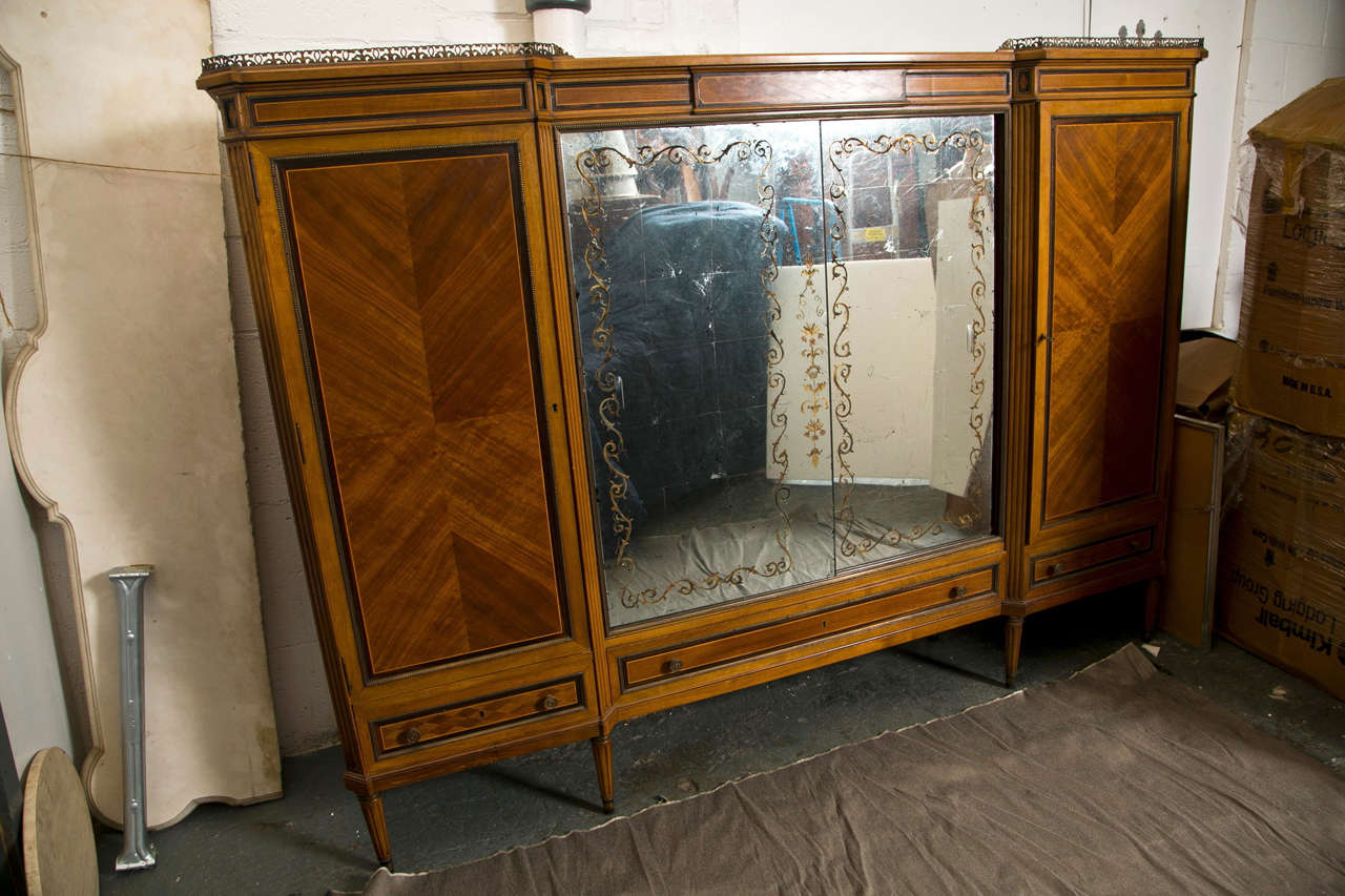 Lovely French Directoire style mahogany, rosewood and satinwood wardrobe cabinet, the top with bronze gallery over a conforming inlaid cabinet fitted with églomisé glass doors flanked by shelving cabinet on each side, banded by bronze borders,