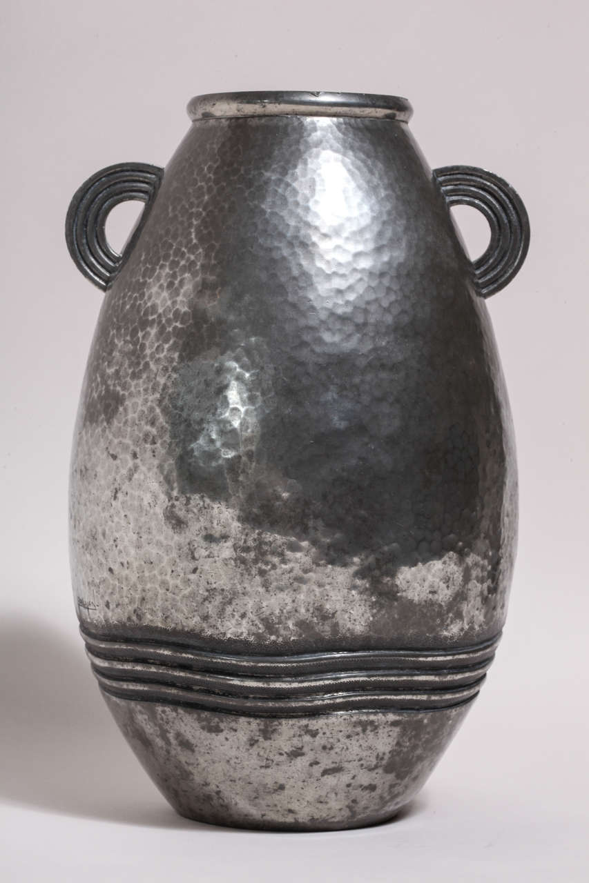 Hand-wrought dinanderie pewter martele´ ovoid vase with waves around the base, martele´ body and two small semi-circular handles at top.
Signed: ''R Delavan'' on body
Stamped: ''R DELAVAN/ DECORATEUR/ PARIS/ ETAIN D'ART'' underside
