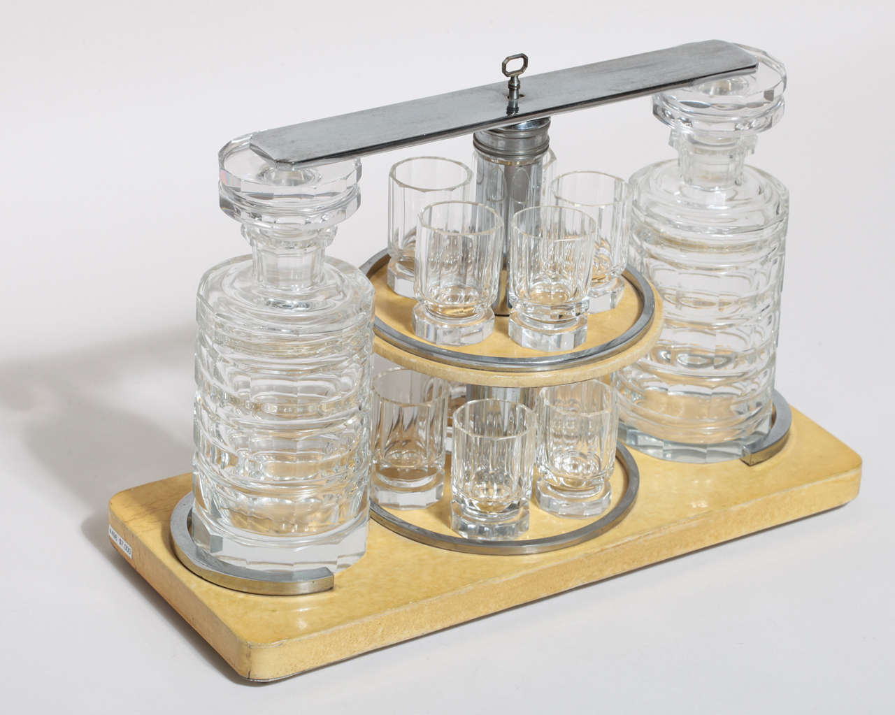 Liquor caddy on parchment covered base and chrome stem with two cut crystal decanters and ten cut crystal glasses. It has a locking bar with original key.