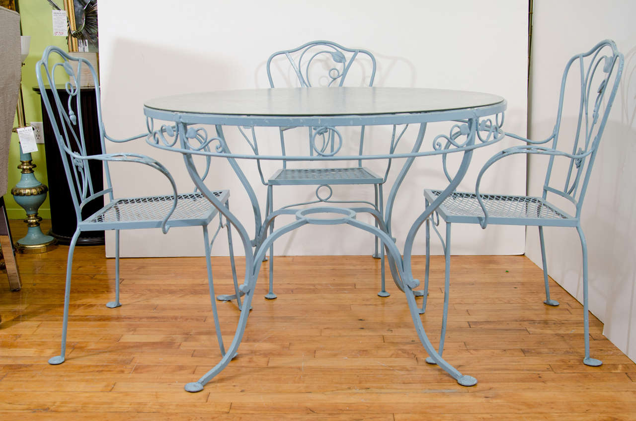 A vintage patio or garden set comprised of a wrought iron table and chairs by Salterini. The table has a tempered glass top and the four chairs and the table are painted light blue and decorated with a floral motif. Signed Salterini on the inside of