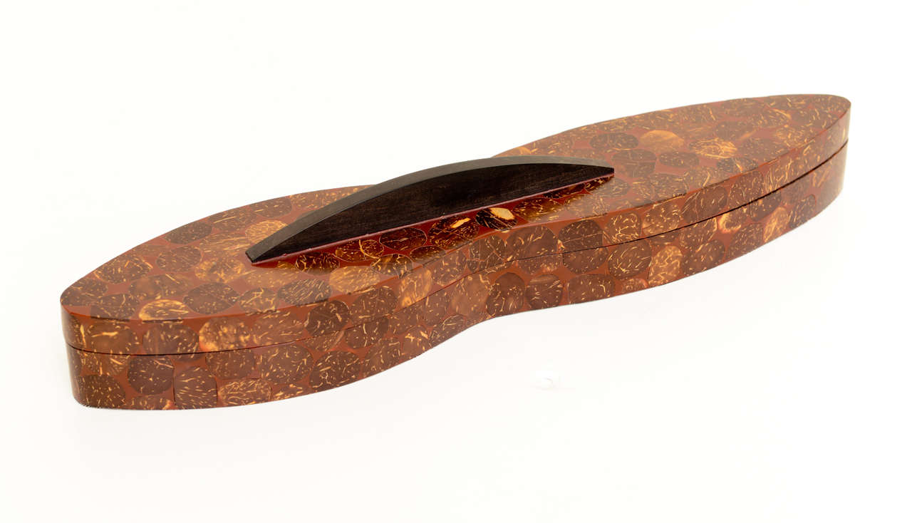 This great elongated 2-part sculptural unusual lidded box has an ebonized wood handle. It is sliced penshell and coconut. This is one of R&Y Augousti's earliest works that is stamped London on the underside. It is very rare. One never sees boxes