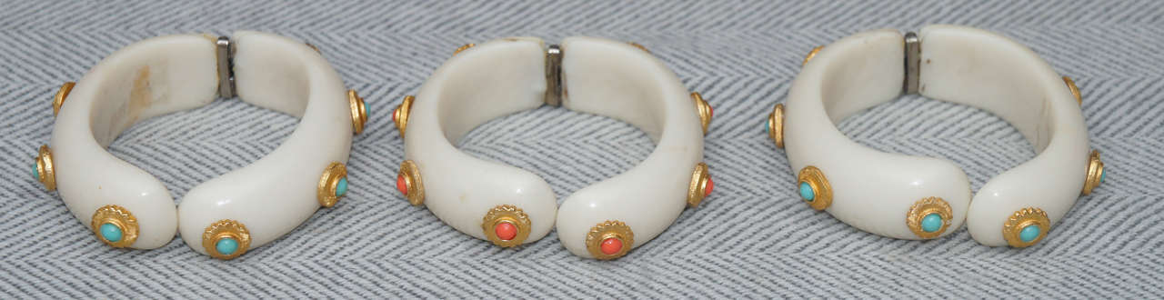 Group of three Hattie Carnegie style faux ivory bangle bracelets. Two inset
with faux turquoise and one with faux coral within gilt metal disks. Hinged
clasps.