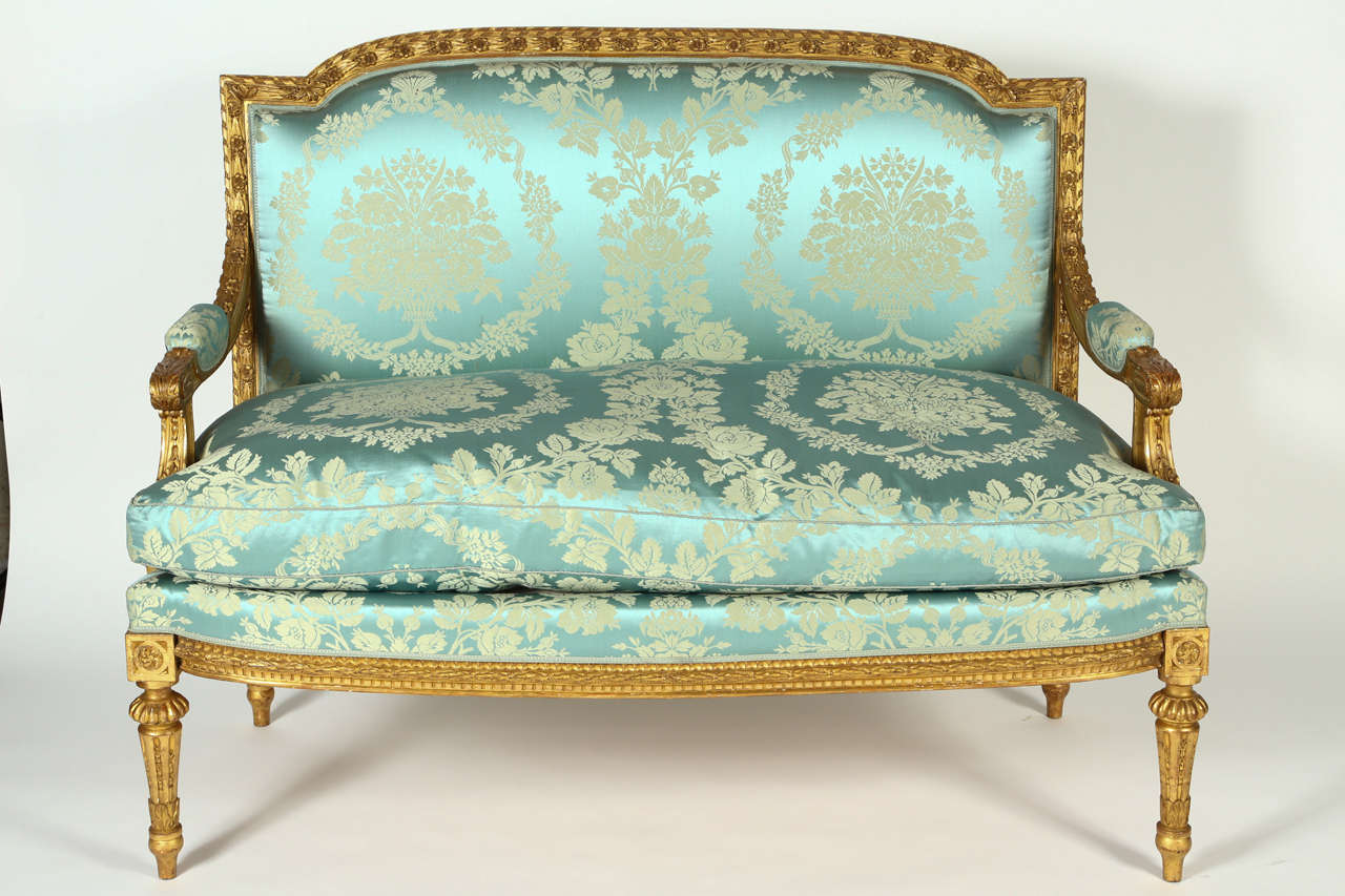 This spectacular French gilt-wood framed sofa is ornately carved with flowers and foliage in the Louis XVI style. The upholstery is a breath-taking, pale blue silk damask. It has padded arms and tapered reeded legs. This piece would make a wonderful