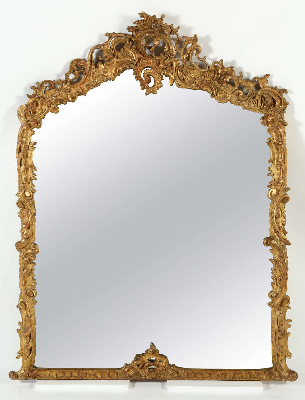 This large giltwood mirror from the 19th century has an arched glass plate within a C-scroll, vigorously carved, floral, foliate and rocaille-decorated crested surround. This mirror has a wonderful balance between simplicity of form and