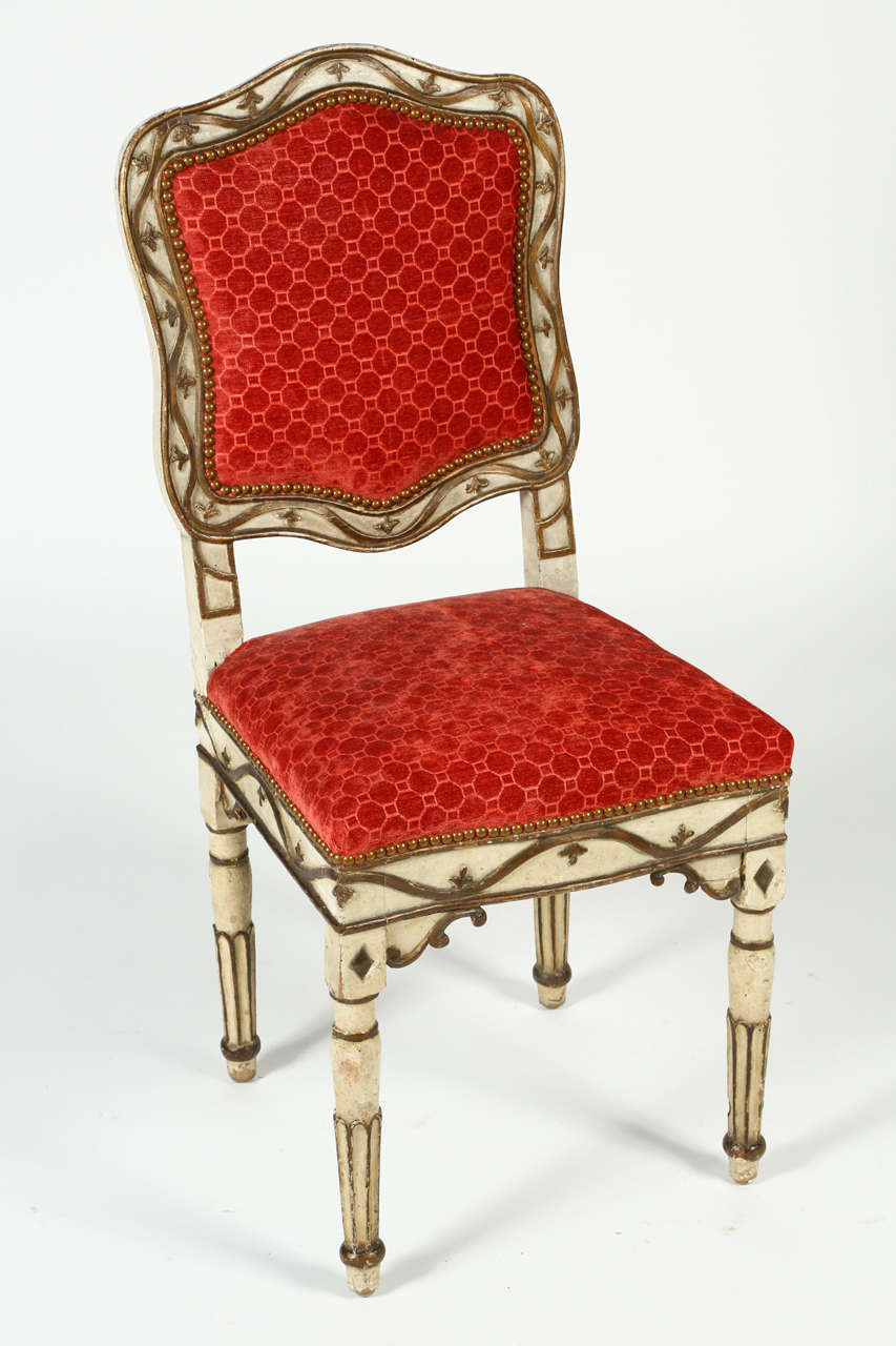 This charming chair from the end of the Louis XVIII period delicately perches on reeded, tapered legs. Parcel-gilt over white paint featuring charming flour de lis details. This show stopper is upholstered in a vibrant red patterned velvet and the