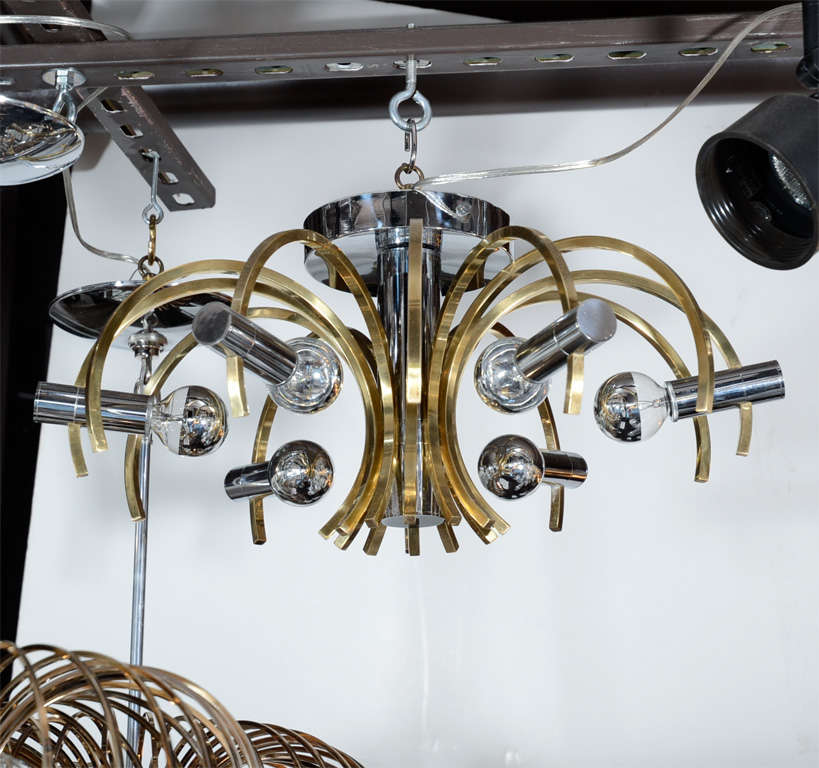This brass and chrome chandelier by Sciolari represents the bold sophistication of 1970s design at its best. It features a chrome cylinder that extends from a circular chrome base. 12 curved brass rods affix to the central cylinder, forming