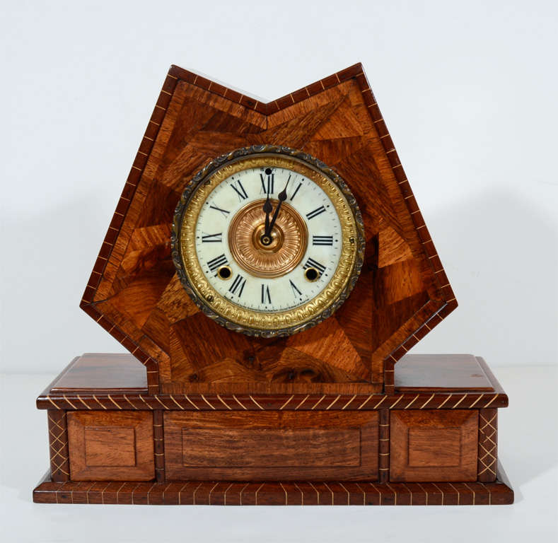 Handsome Arts and Crafts inlaid geometric, tortoise design exotic wood mantle clock features a reverse gilt and enamel dial, bias-striped trim and two secret drawers. Has been converted to battery operation for convenience.