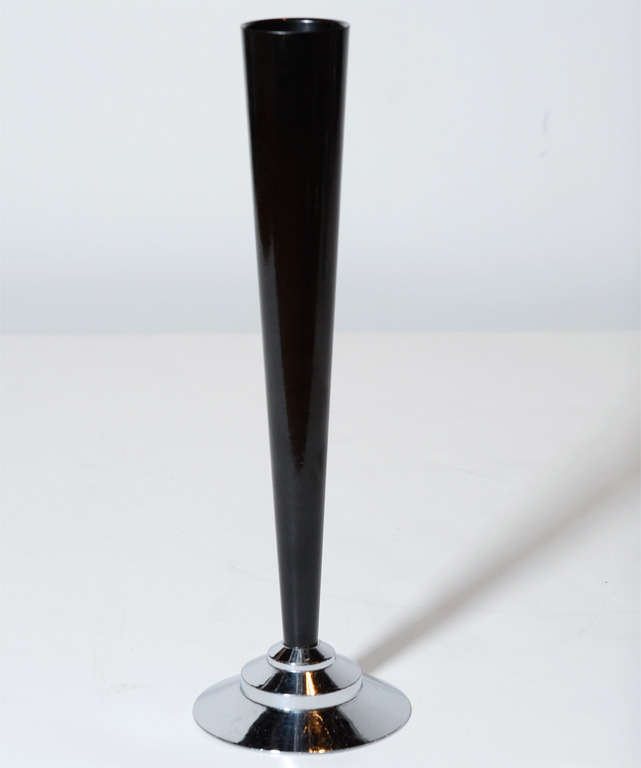 This stunning Art Deco Machine Age bakelite bud vase features a slender conical body realized in black bakelite that rests atop a stepped skyscraper style base in lustrous chrome. While this is a perfectly functional item- ideal for presenting