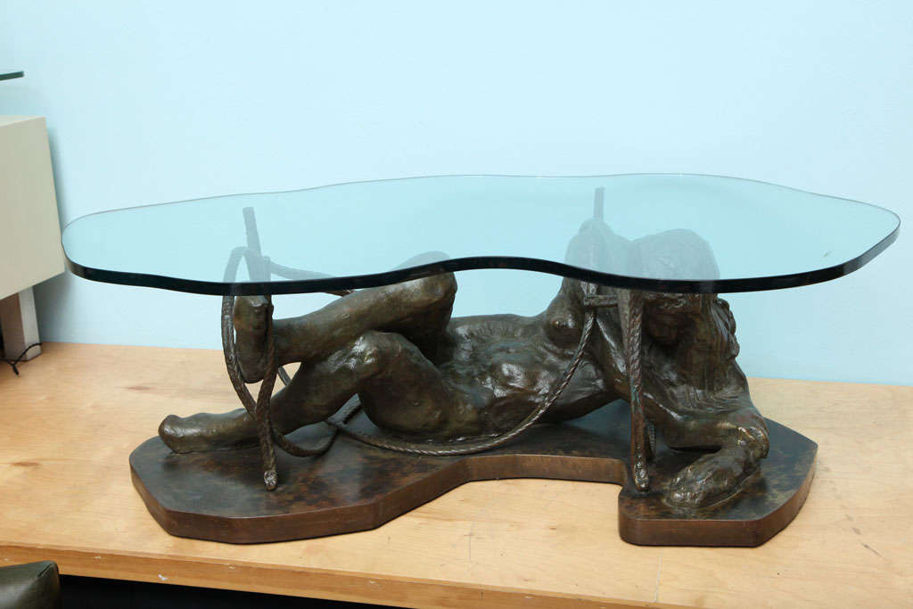 Moody and beautiful cast-bronze base in the form of a reclining woman on a shaped plinth.  Entwining bronze rope surrounds the figure, & supports a free form glass top.  Signed on base.  From an edition of no more than 4.