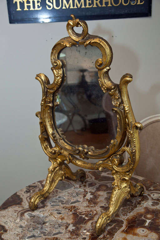 We love this little beauty for its elegant, yet rococo, hand-carved wooden frame, original glass, and early 20th C folksy re-gilded surface that adds a note of whimsy.  The mirror rocks in its frame, so it can be angled to your best advantage. 