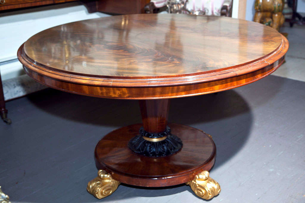 Tilt-top above a tapering base ending in black painted acanthus leaves and gilt, over a circular base raised on gilt carved feet.
 