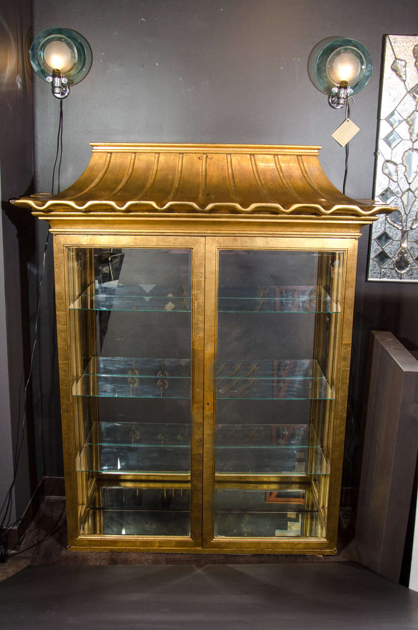 Rare and outstanding illuminated vitrine or display cabinet in antique gold leaf finish. The cabinet has an Asian inspired design with pagoda top detail. The cabinet can be wall mounted if desired. It is made of hand carved wood with hand painted