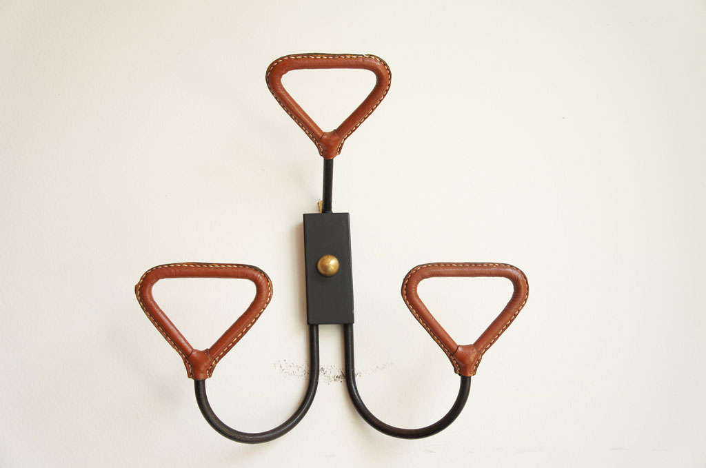 wonderful three arm coat hanger by designer, Jacques Adnet in saddle leather with contrast stitching, set on an iron base.
